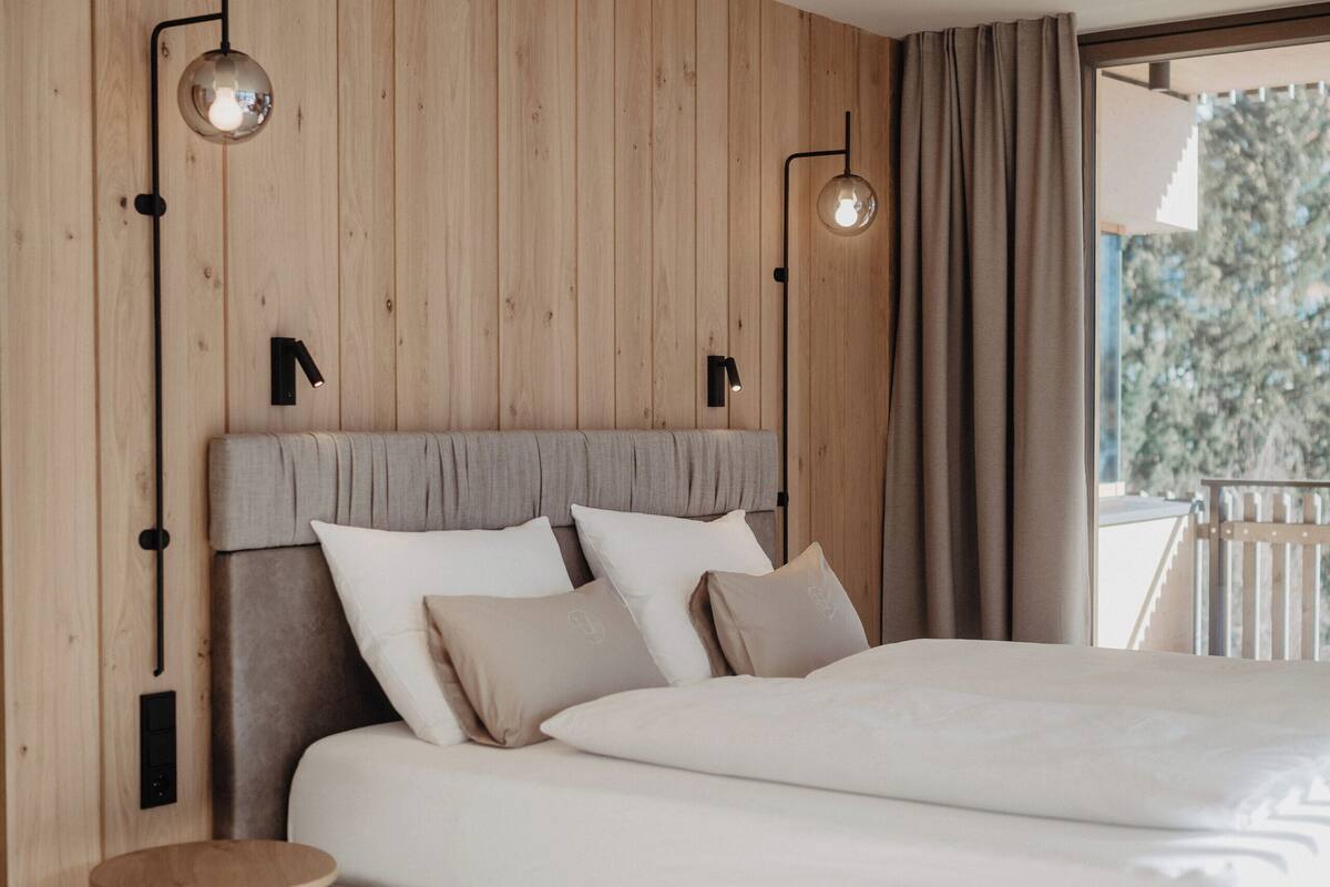 A modern bedroom with a large bed, wooden panel walls, and two wall-mounted lights.