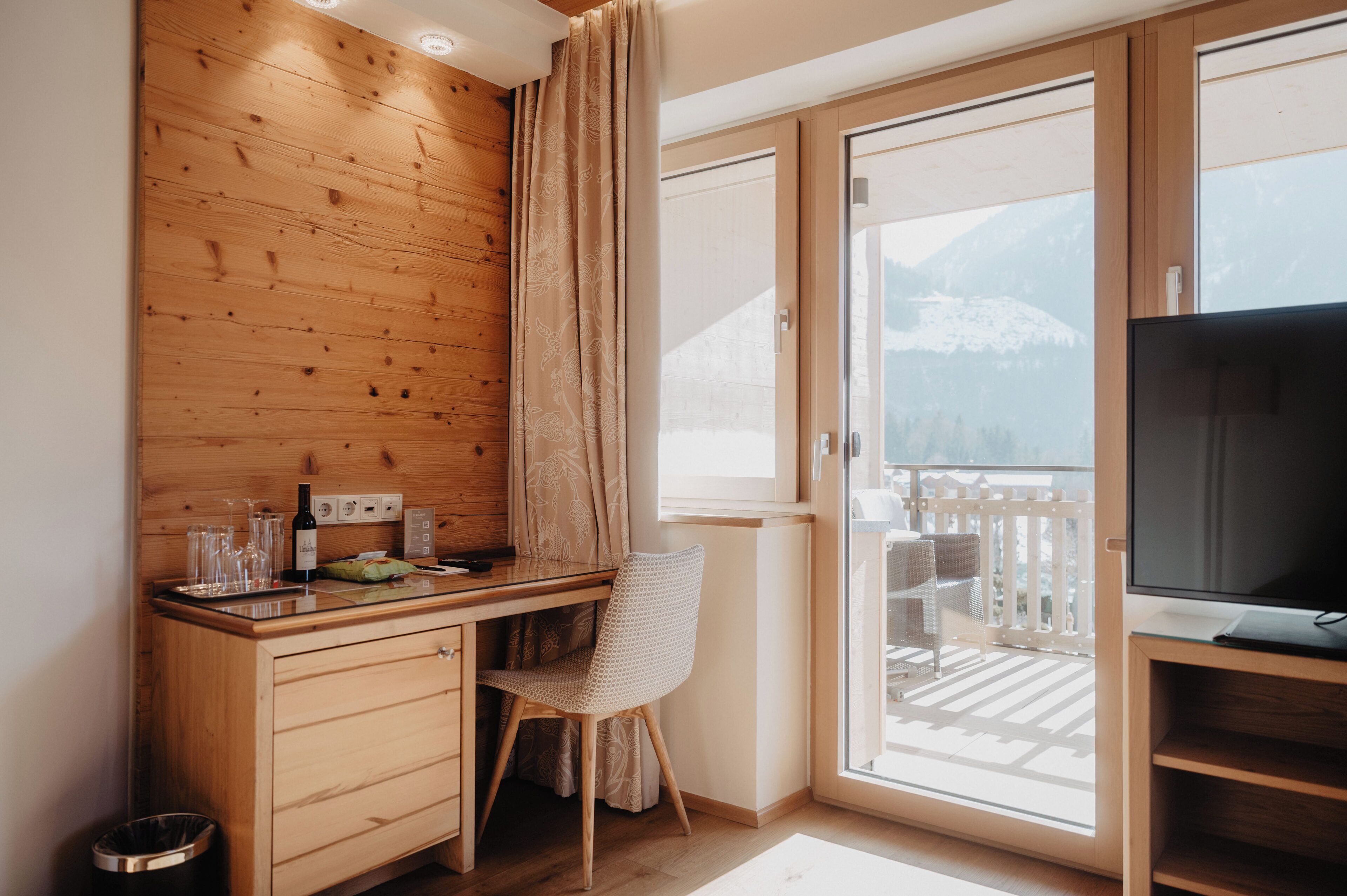 A wooden desk with a chair, a TV, and a window with a mountain view.