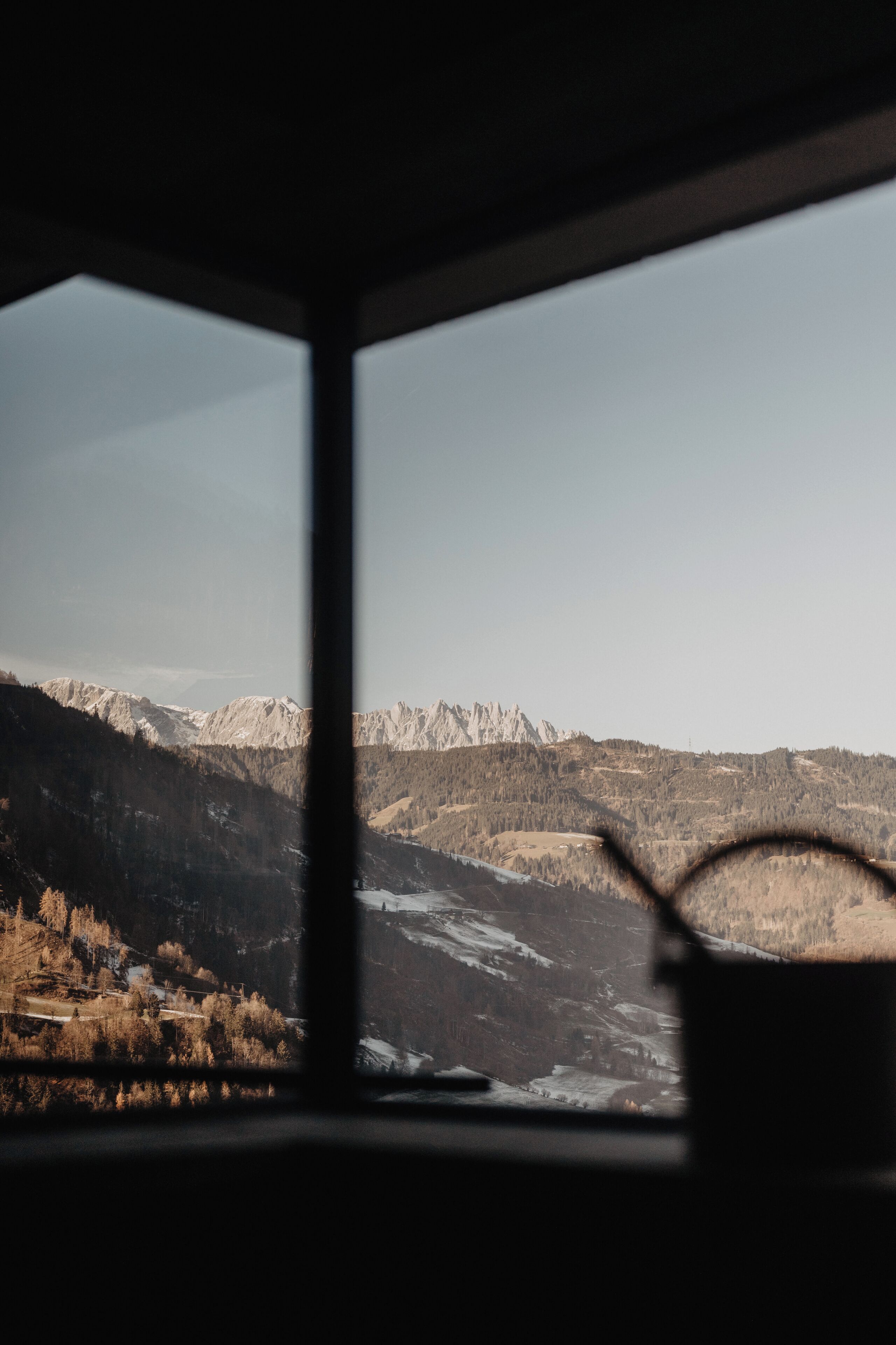 Une vue à travers une fenêtre sur un paysage de montagne, avec des sommets enneigés et une vallée.
