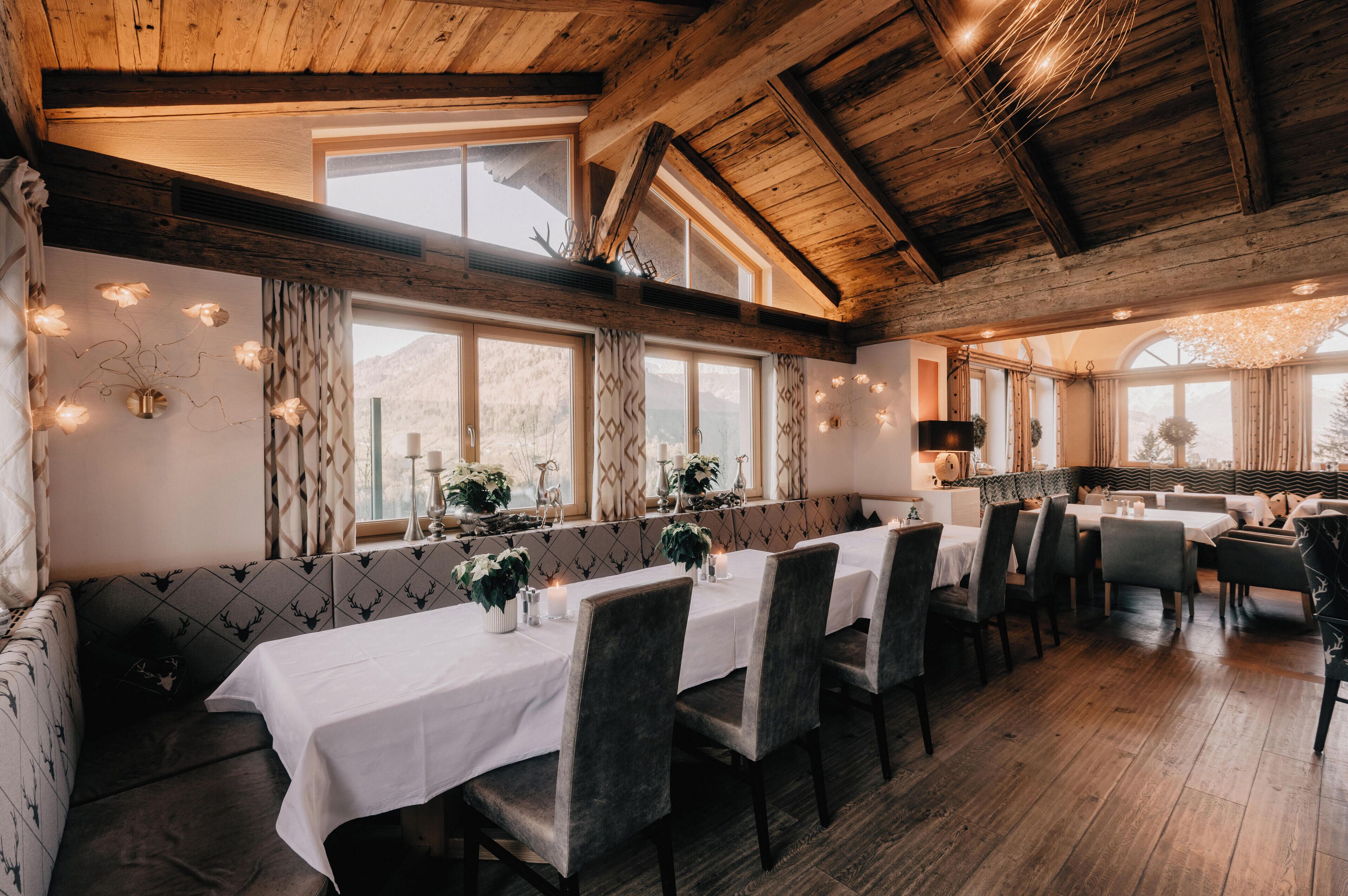 A restaurant with wooden beams, large windows, and a long dining table with chairs.