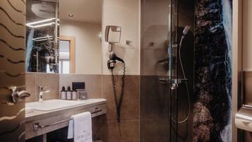 Ein modernes Badezimmer mit Waschtisch, großem Spiegel, Haartrockner und Dusche mit Wasserfall-Motiv.