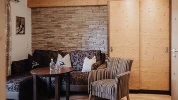 Une pièce chaleureuse avec un mur en bois, un canapé, un fauteuil à rayures et une petite table ronde sur laquelle se trouvent une bouteille et des verres.