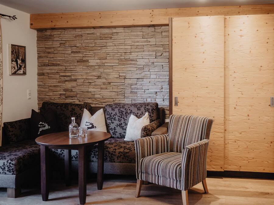 Une pièce chaleureuse avec un mur en bois, un canapé, un fauteuil à rayures et une petite table ronde sur laquelle se trouvent une bouteille et des verres.