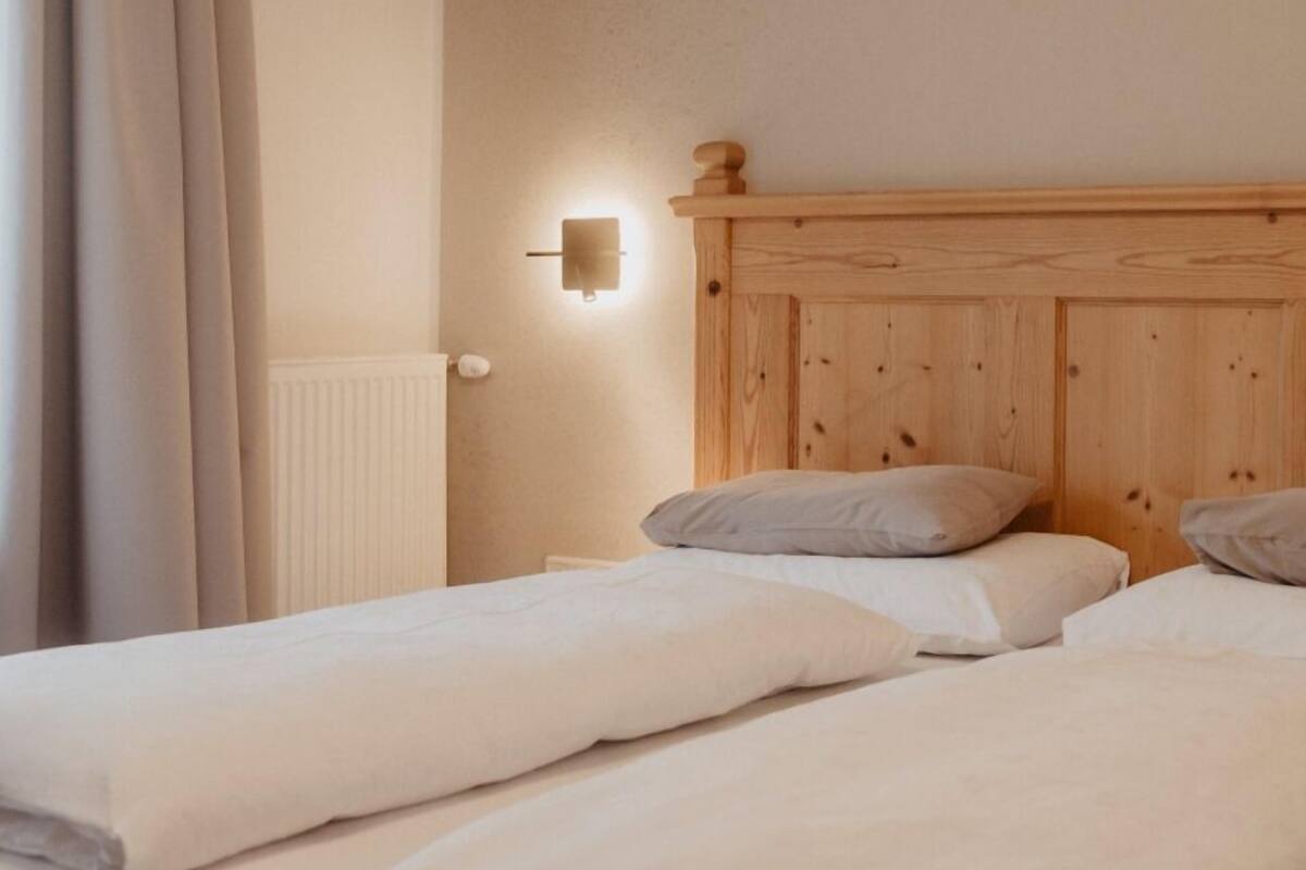 A double bed with wooden headboard, white linens, and a wall-mounted light fixture.