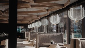 A modern restaurant interior with high ceilings, patterned seating, and hanging light fixtures. -  Hotel Berghof | St. Johann in Salzburg (Sankt Johann im Pongau)