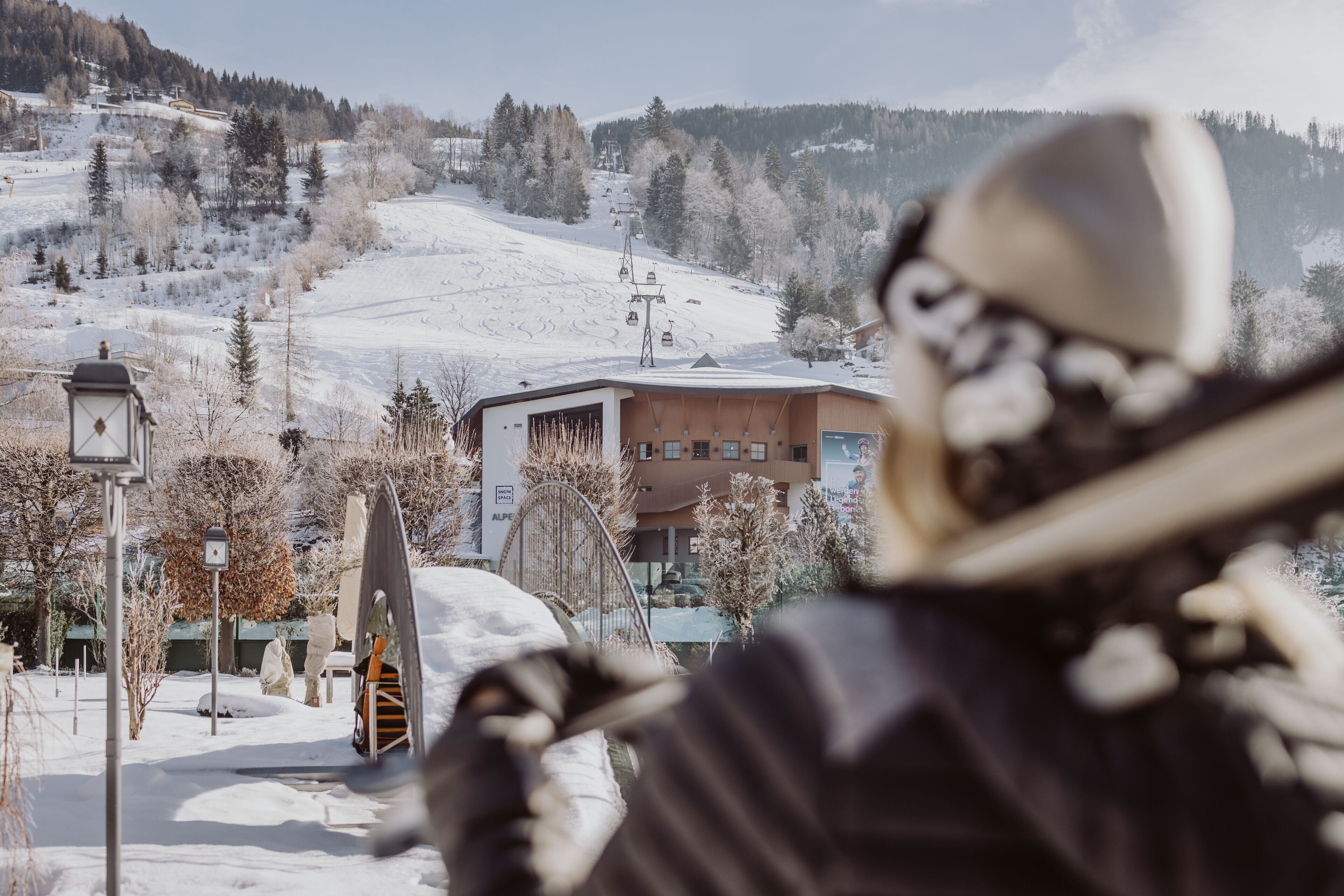 Estância de esqui com teleférico, edifícios e árvores cobertas de neve.