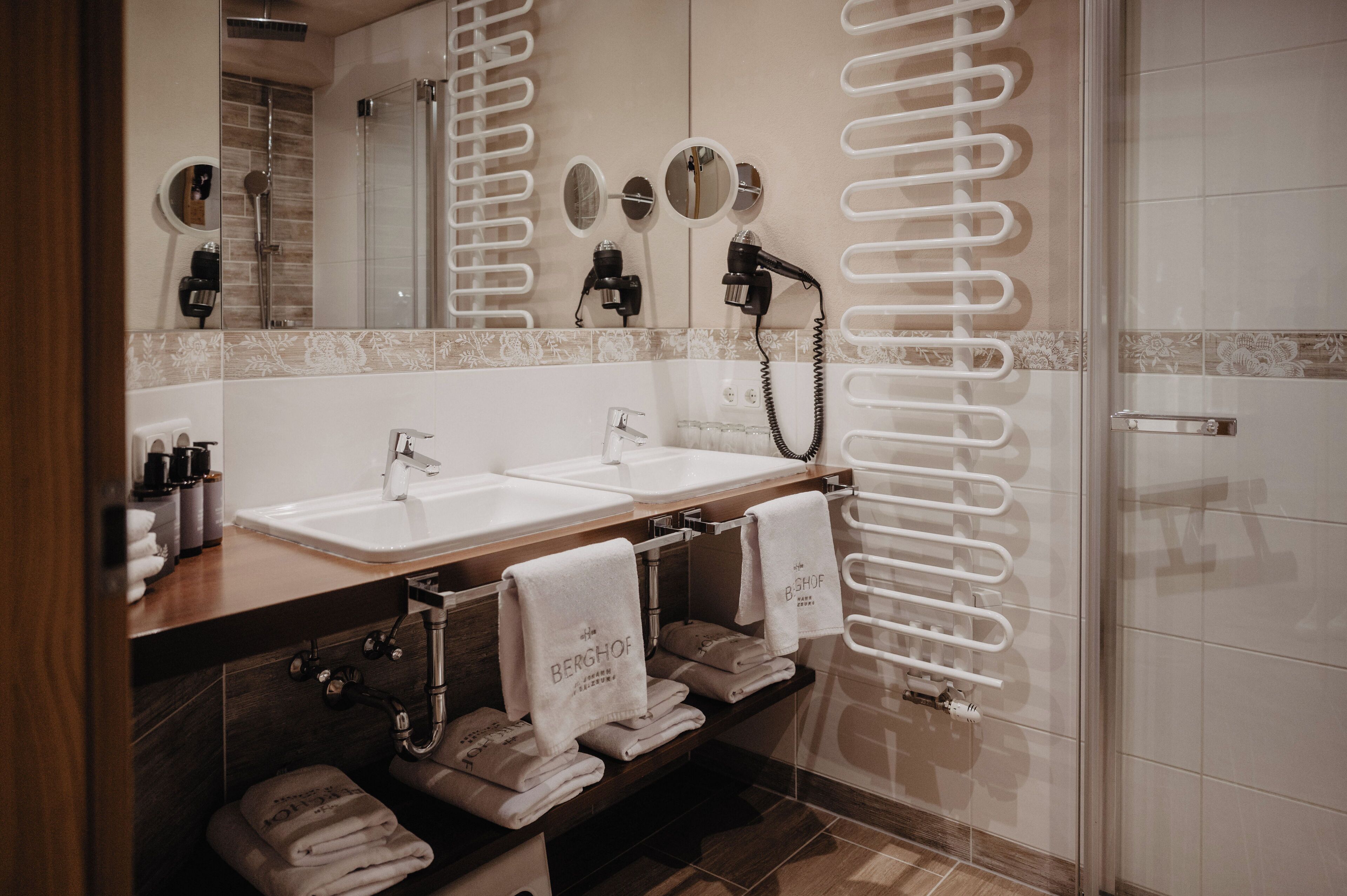 Ein modernes Badezimmer mit zwei Waschbecken, einem Spiegel, einem Handtuchhalter und einer Duschkabine.