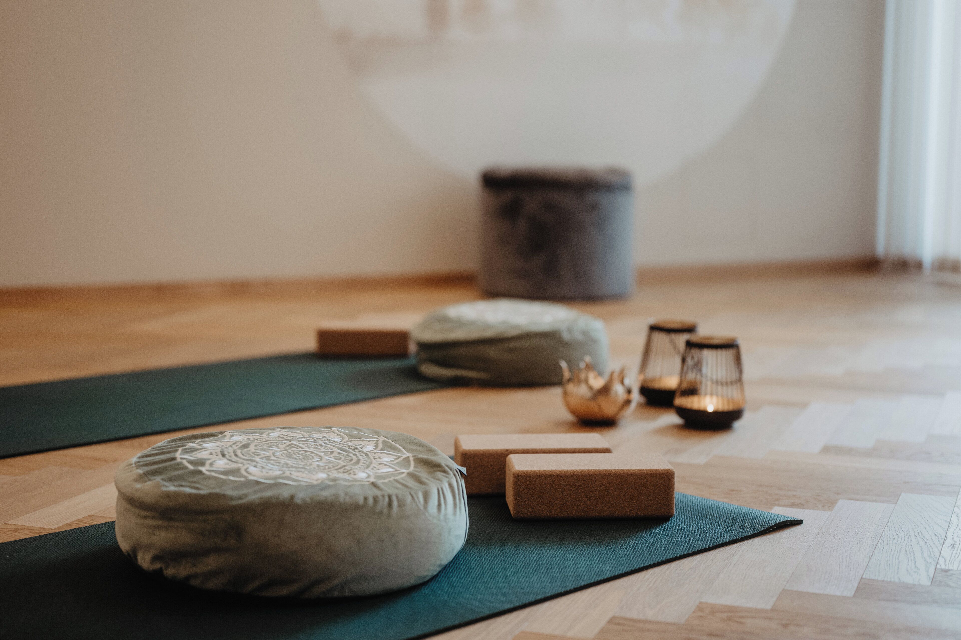 Una esterilla de yoga con un cojín y un taburete de madera pequeño en una habitación con suelo de madera.