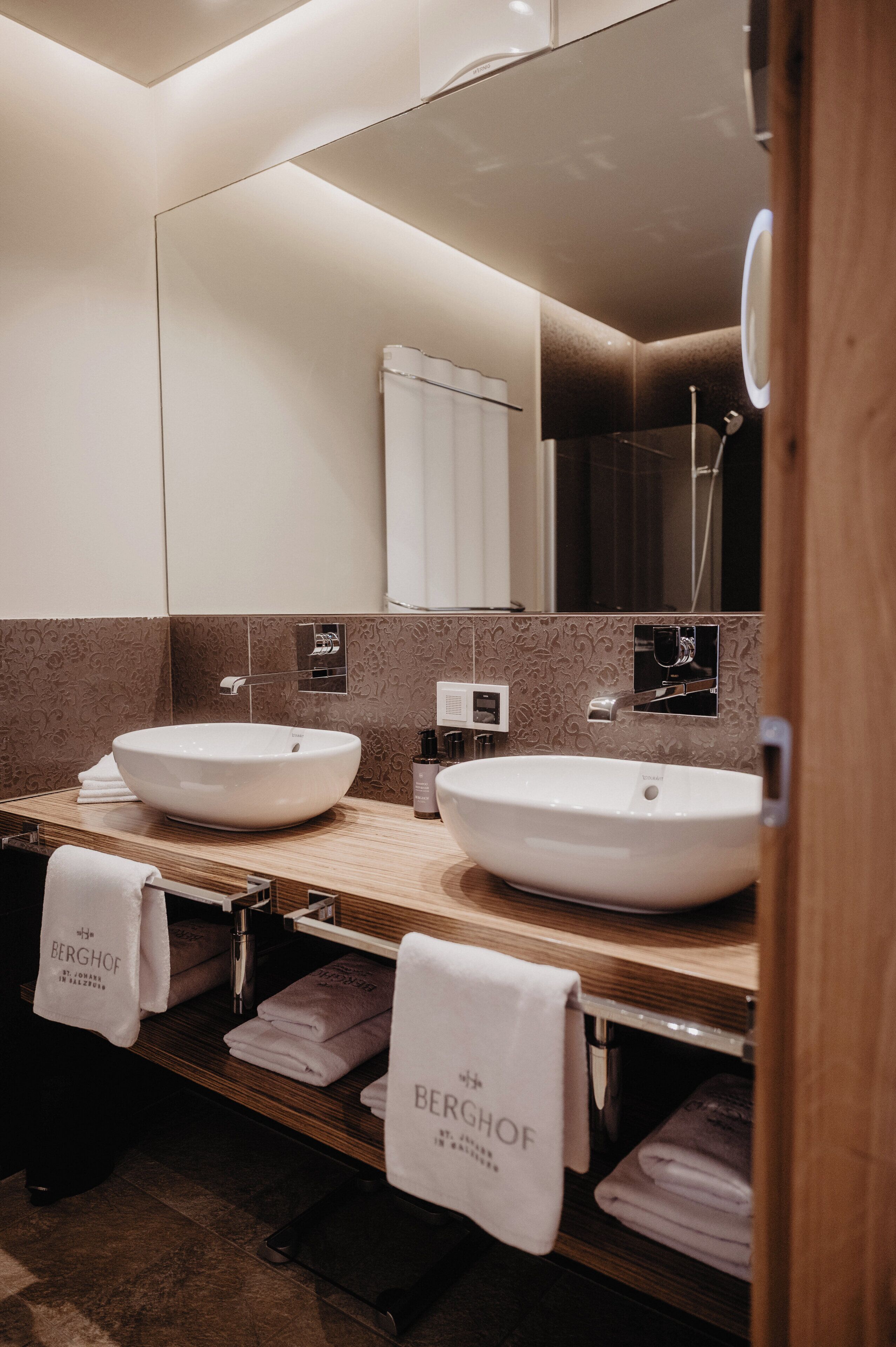Une salle de bain moderne avec deux lavabos, un grand miroir et des serviettes portant la marque « BERGHOF ».