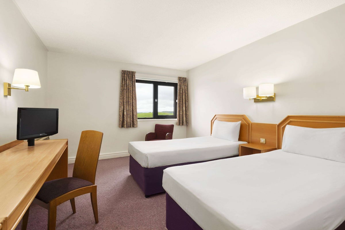 Une chambre d’hôtel avec deux lits, un bureau, une chaise et un téléviseur.