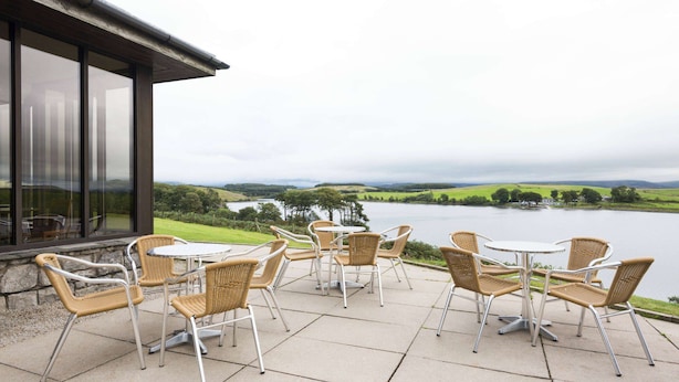 Une terrasse extérieure avec des chaises et une table en osier, offrant une vue sur un lac et des collines lointaines.