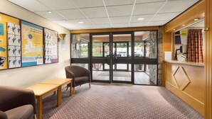 Un espace d’accueil avec un bureau en bois, une chaise marron, un tapis à motifs et une porte en verre donnant sur l’extérieur.