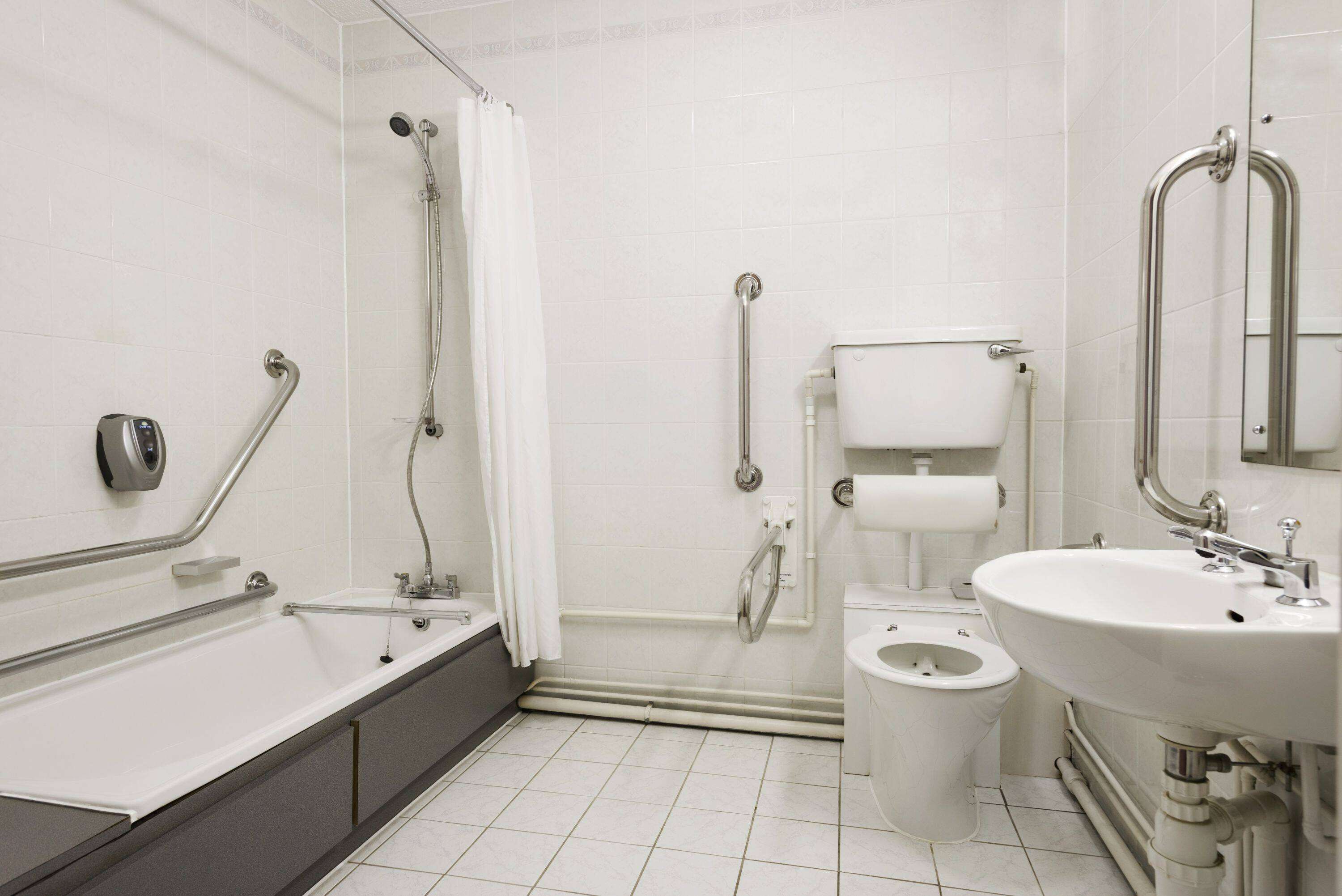A modern bathroom with a bathtub, toilet, and sink, equipped with grab bars and a shower.