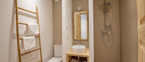 A bathroom with a toilet, a sink with a mirror, a shower, and a towel rack.