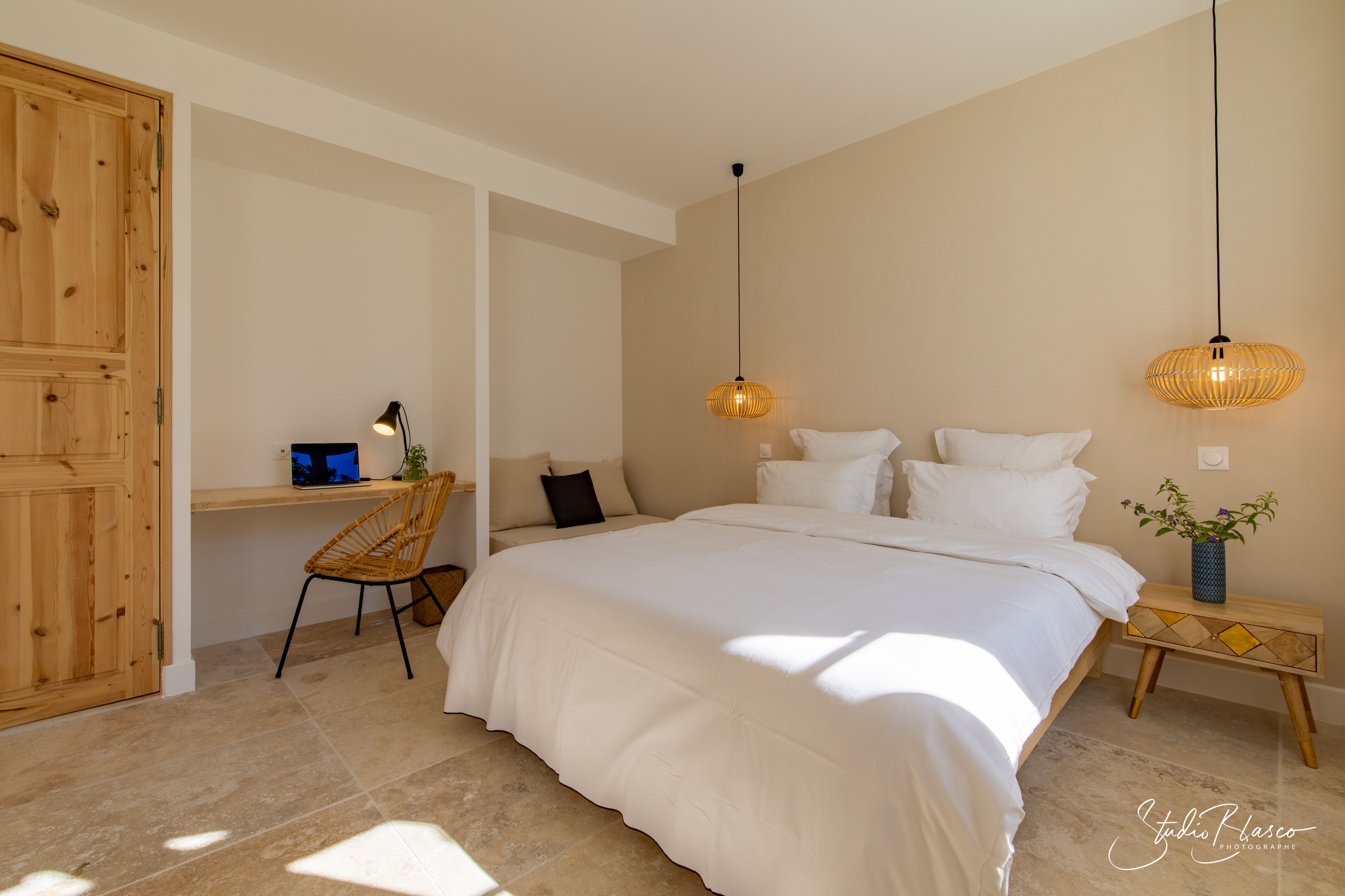 A bedroom with a large bed, a wooden desk, a chair, and two hanging lamps.