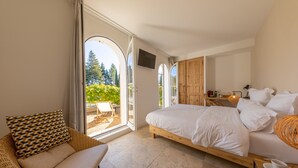 Een slaapkamer met een groot bed, een rieten stoel, een televisie en uitzicht op de omgeving.