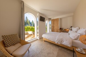 Un dormitorio con una cama grande, una silla de mimbre, un televisor y vistas al exterior.