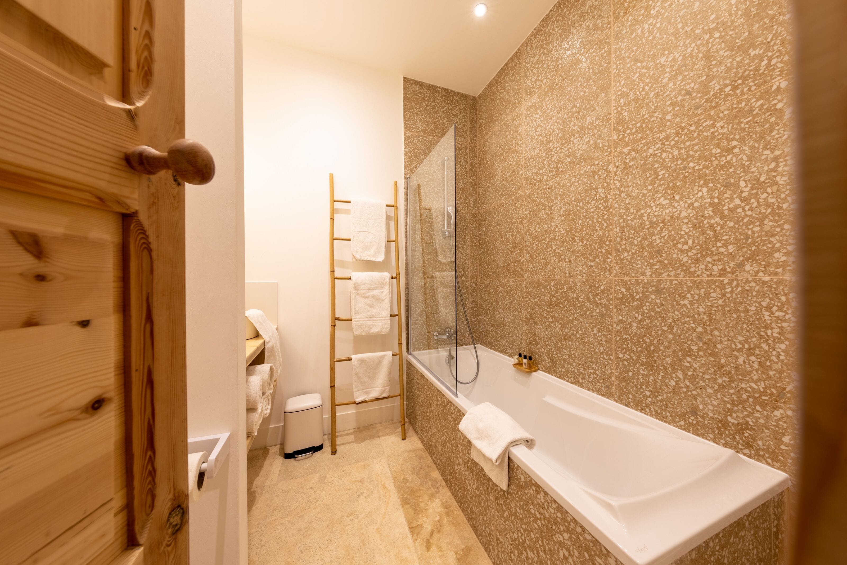 A bathroom with a glass shower enclosure, a white bathtub, and a wooden door.
