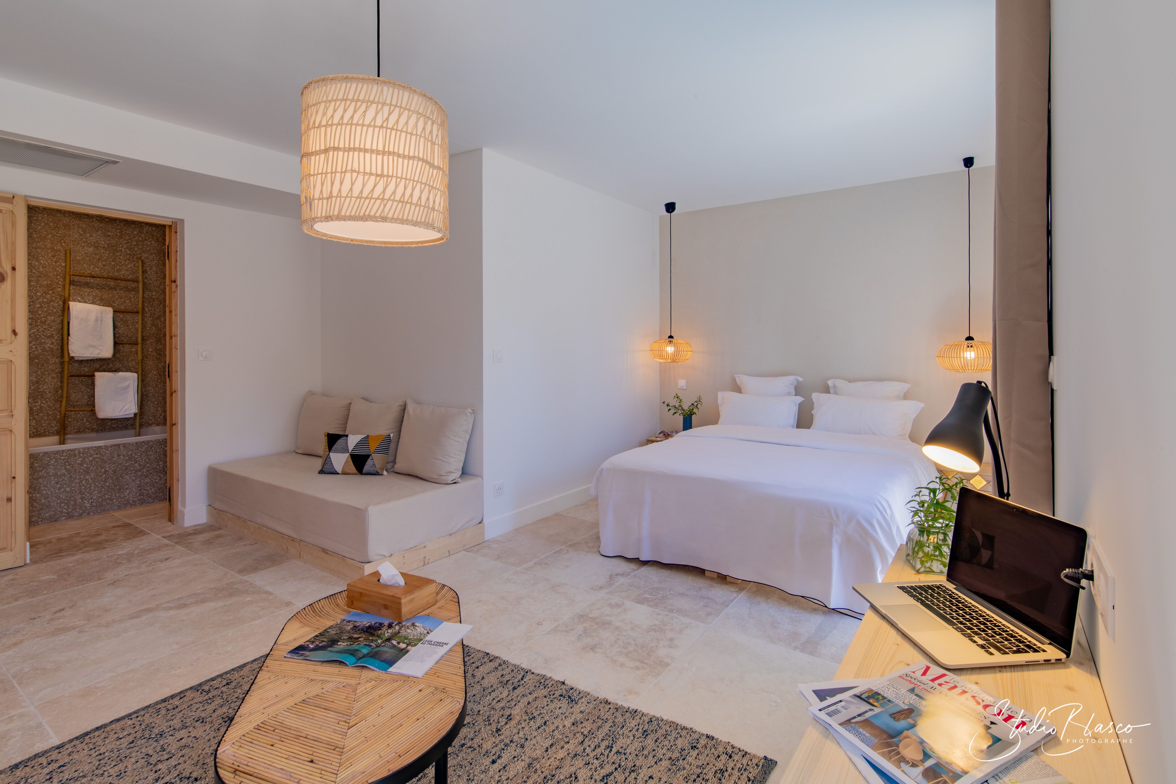 A modern bedroom with a bed, a desk with a laptop, a wooden ladder, and a hanging light fixture.