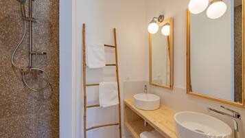 A bathroom with a freestanding shower, a wooden ladder, a round sink, and a large mirror with lights.