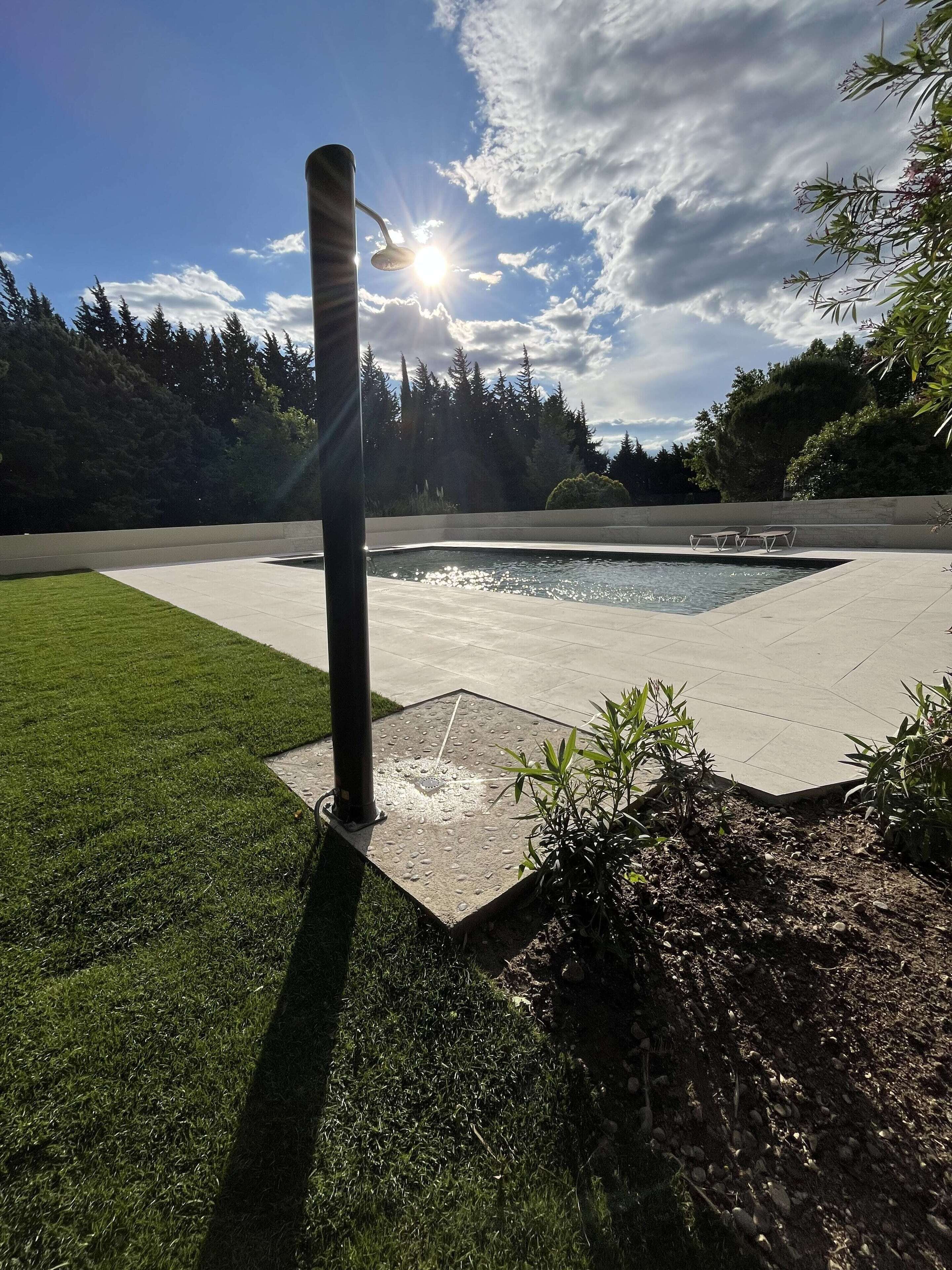 Une piscine entourée d’une zone pavée, avec un poteau en métal et une pelouse.