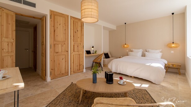 Een moderne slaapkamer met een groot bed, houten deuren, een ronde salontafel met een plant en twee hanglampen.
