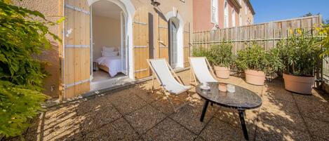 A patio with two lounge chairs, a table, and a wooden door leading to a room.