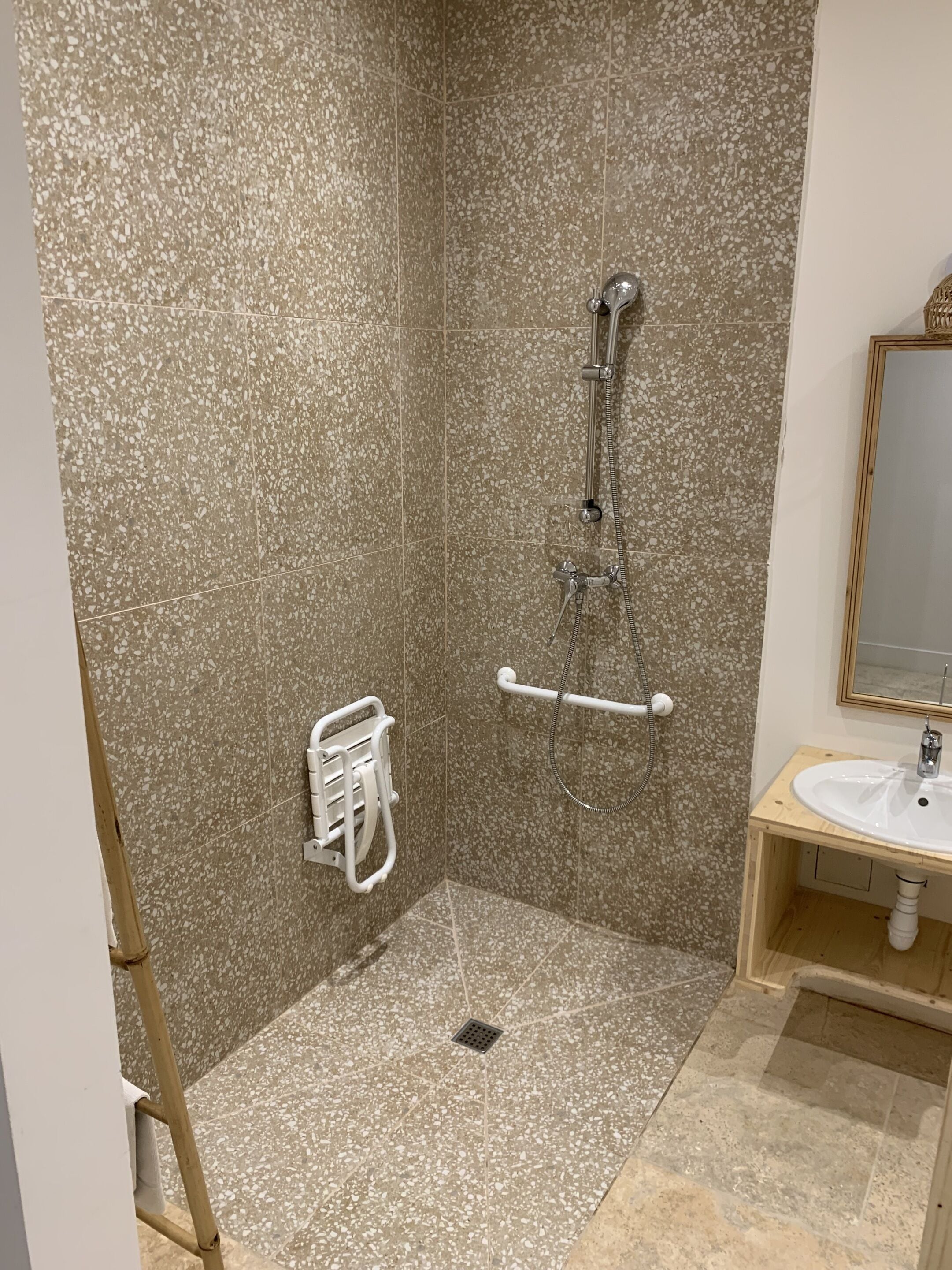 A bathroom with a shower, a handrail, a grab bar, a sink, and a mirror.