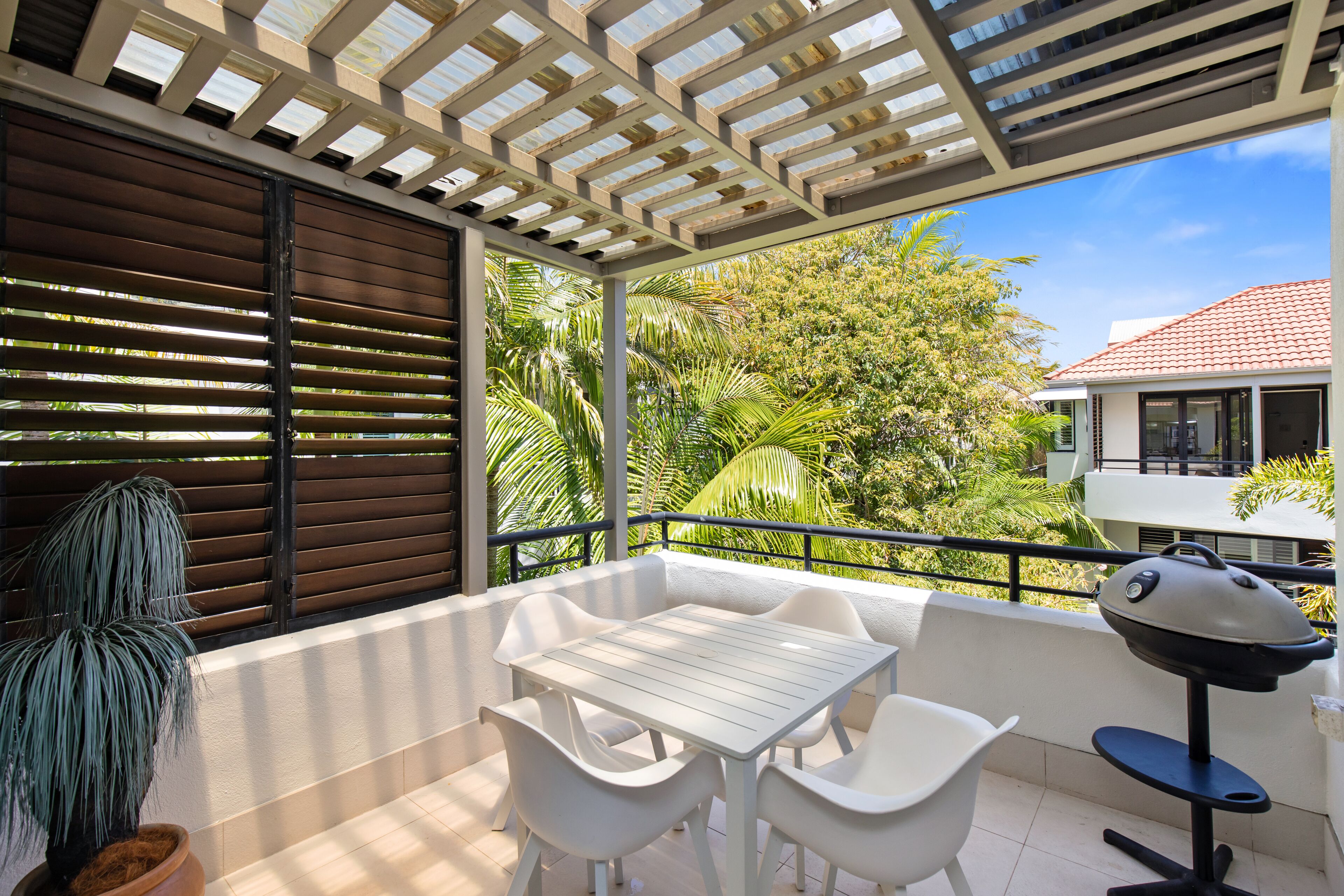 A balcony with a white table and chairs, a barbecue grill, and a potted plant.