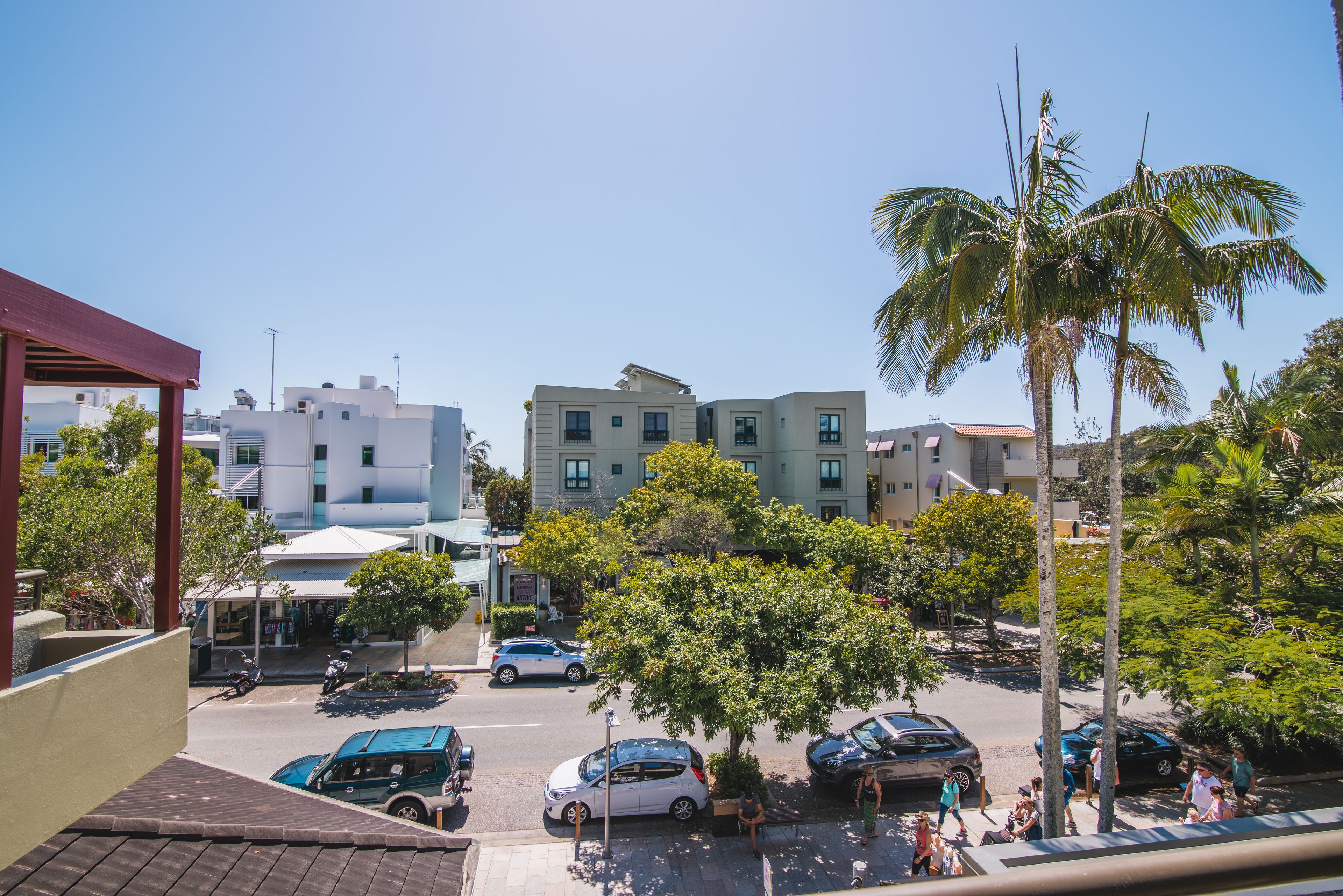 A residential area with modern buildings, parked cars, and palm trees.
