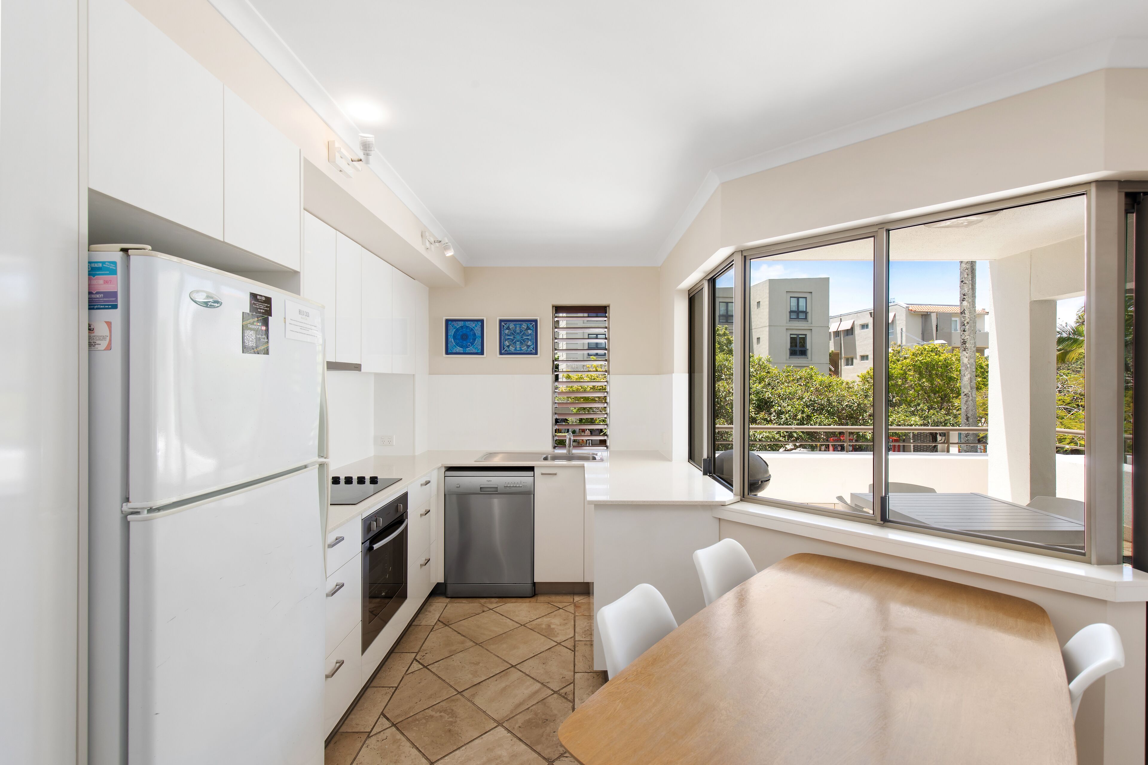 A modern kitchen with white cabinets, a refrigerator, dishwasher, and a dining area with a table and chairs.