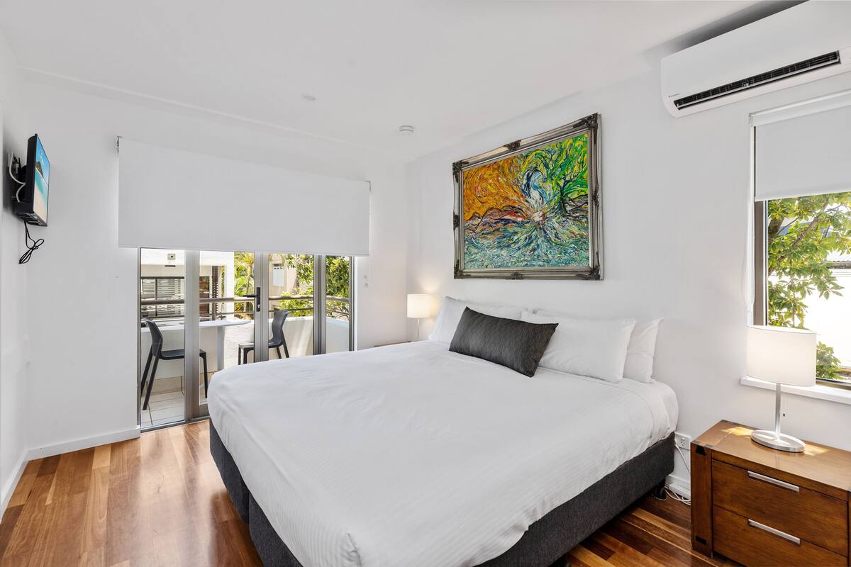A modern bedroom with a large bed, a painting, a desk, and a balcony.