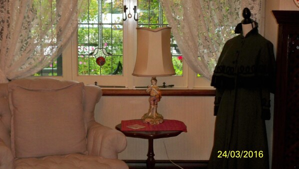 A room with a window, a lamp, a small table, a chair, and a mannequin.
