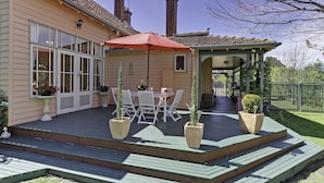 Une terrasse couverte avec une table et des chaises, des plantes en pot et un parasol rouge.
