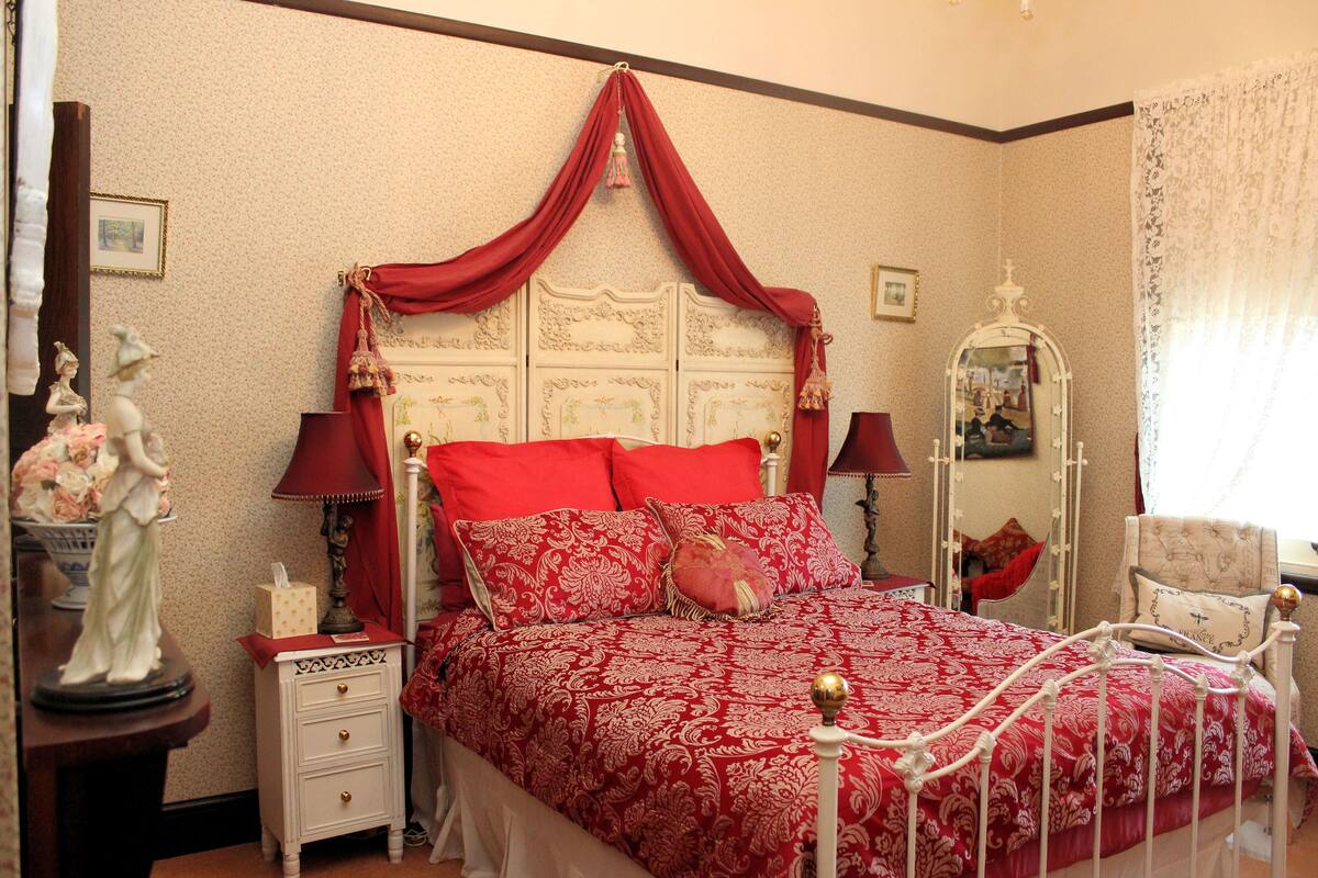 Een slaapkamer met een hemelbed, nachtkastje, dressoir en spiegel.