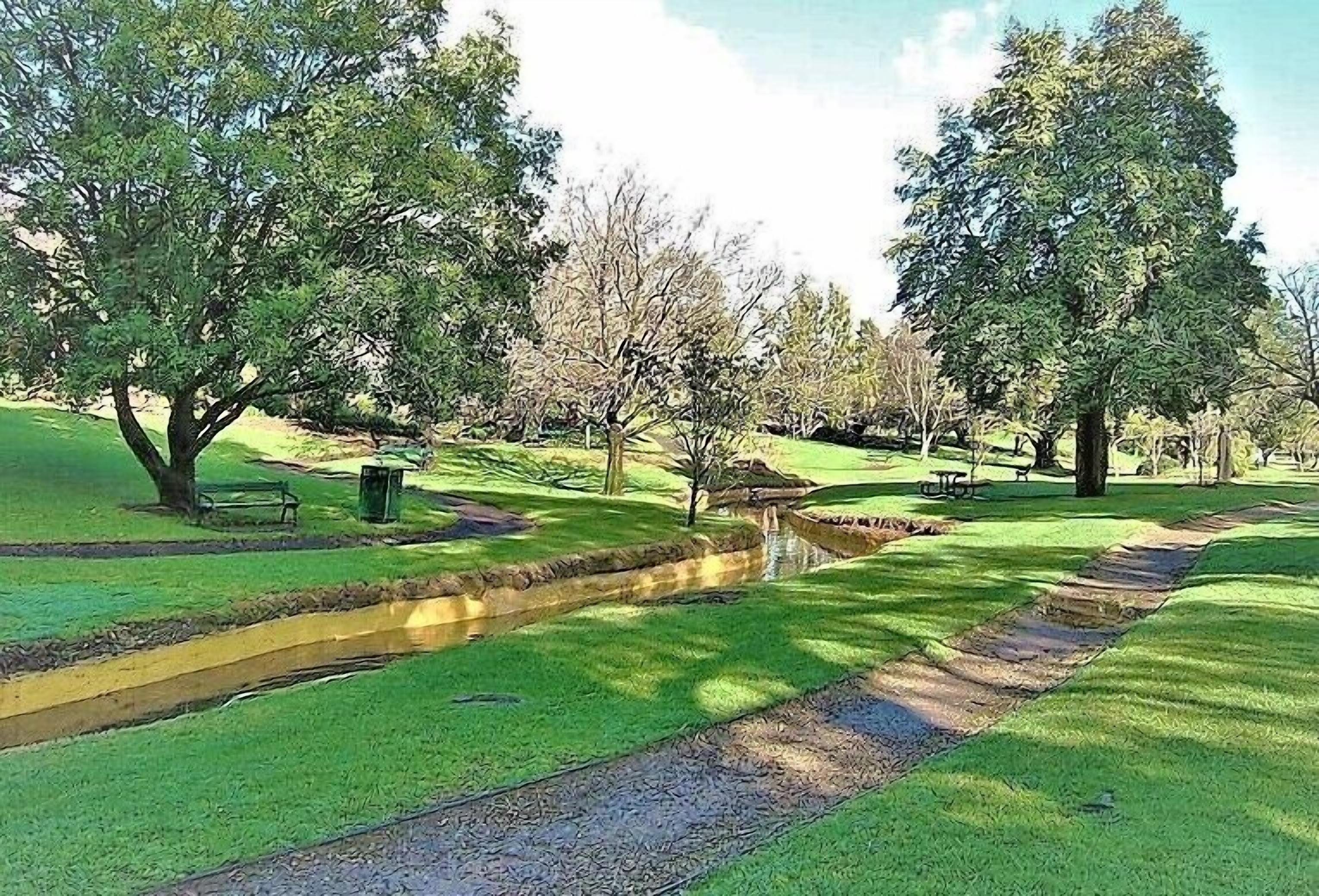A park with a paved path, benches, and trees.