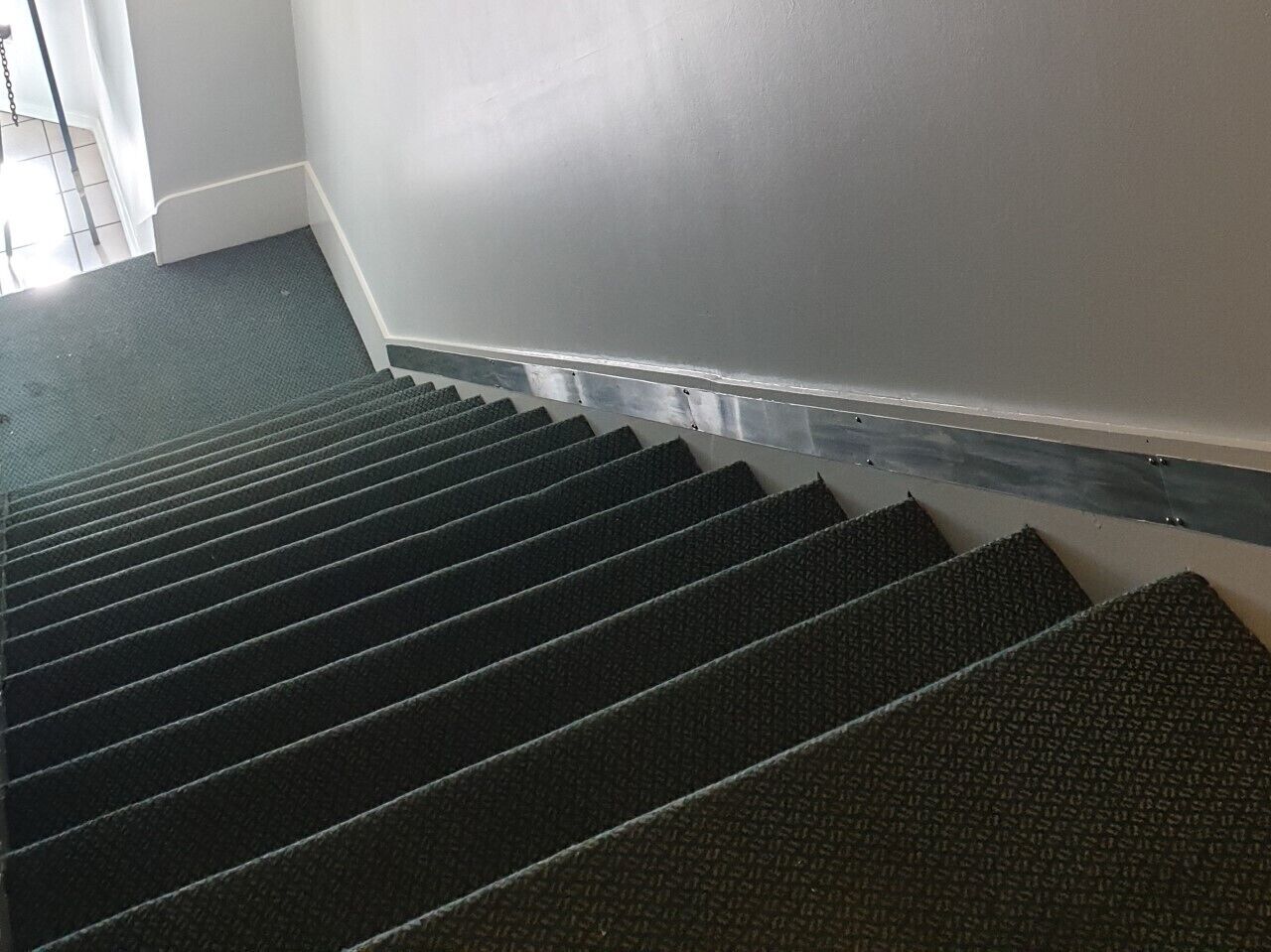 Una escalera con superficie cubierta de alfombra oscura y barandillas metálicas.