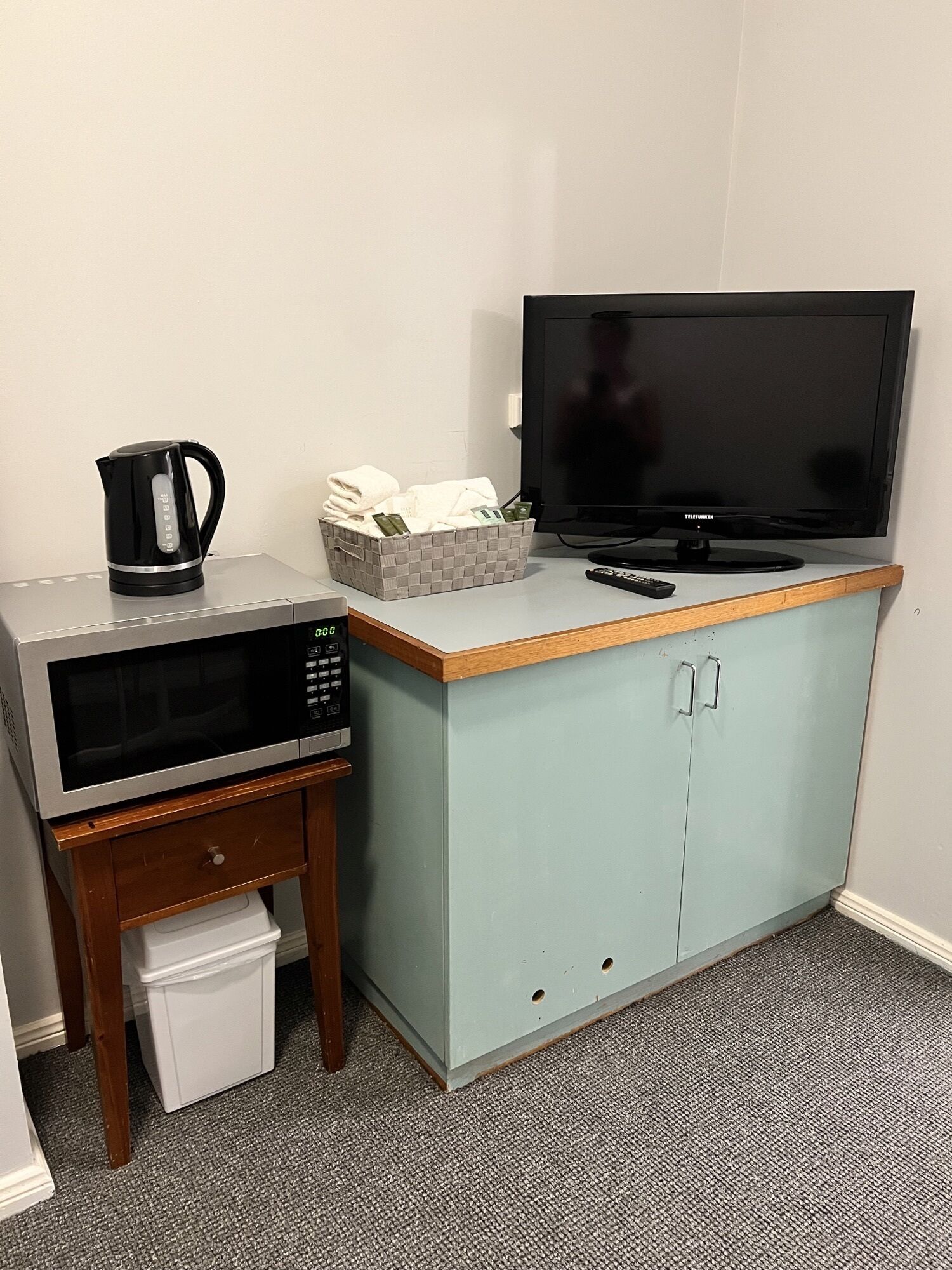 A kitchenette with a microwave, kettle, and a TV on a cabinet.