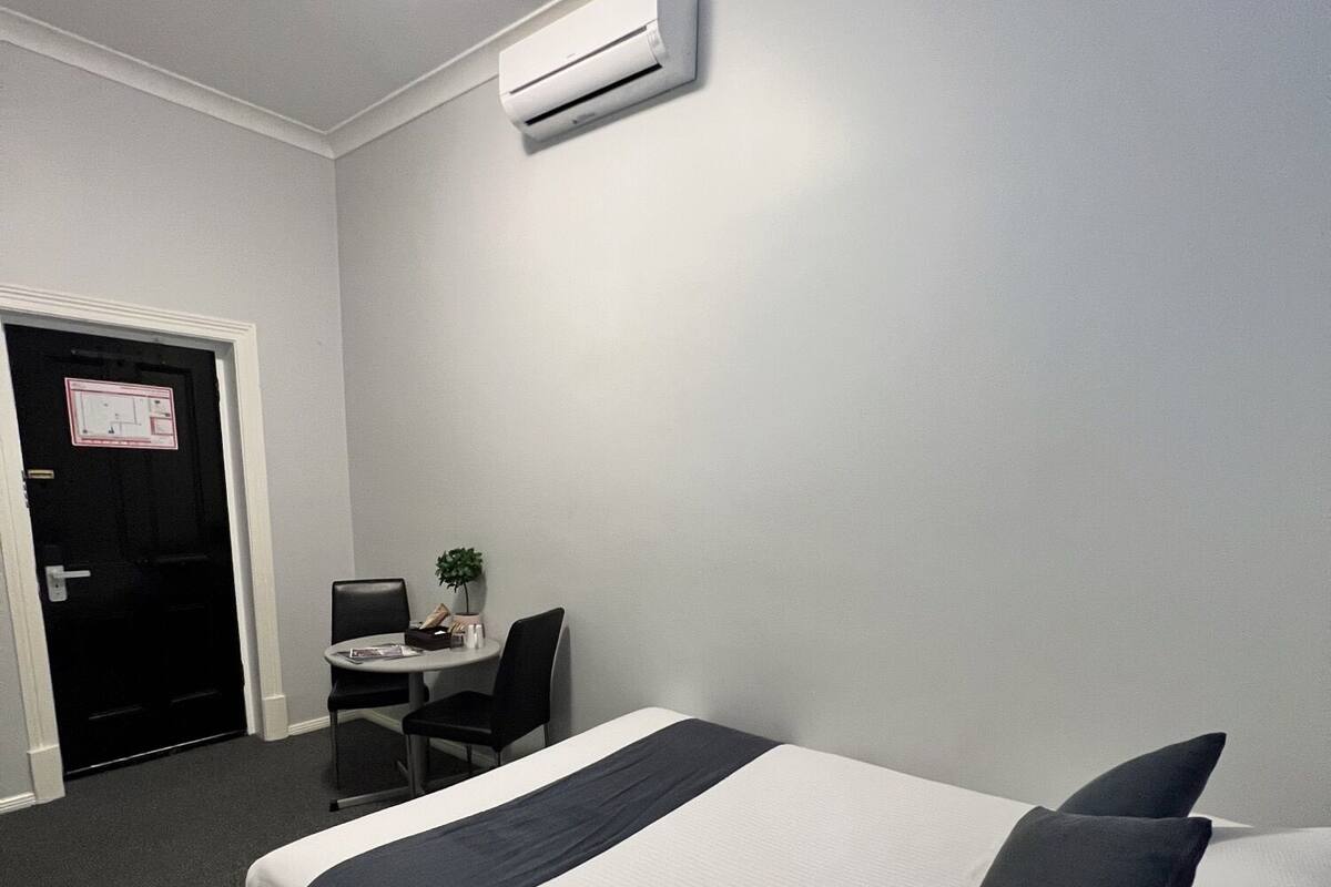 A hotel room with a bed, a desk, a chair, and an air conditioning unit on the wall.