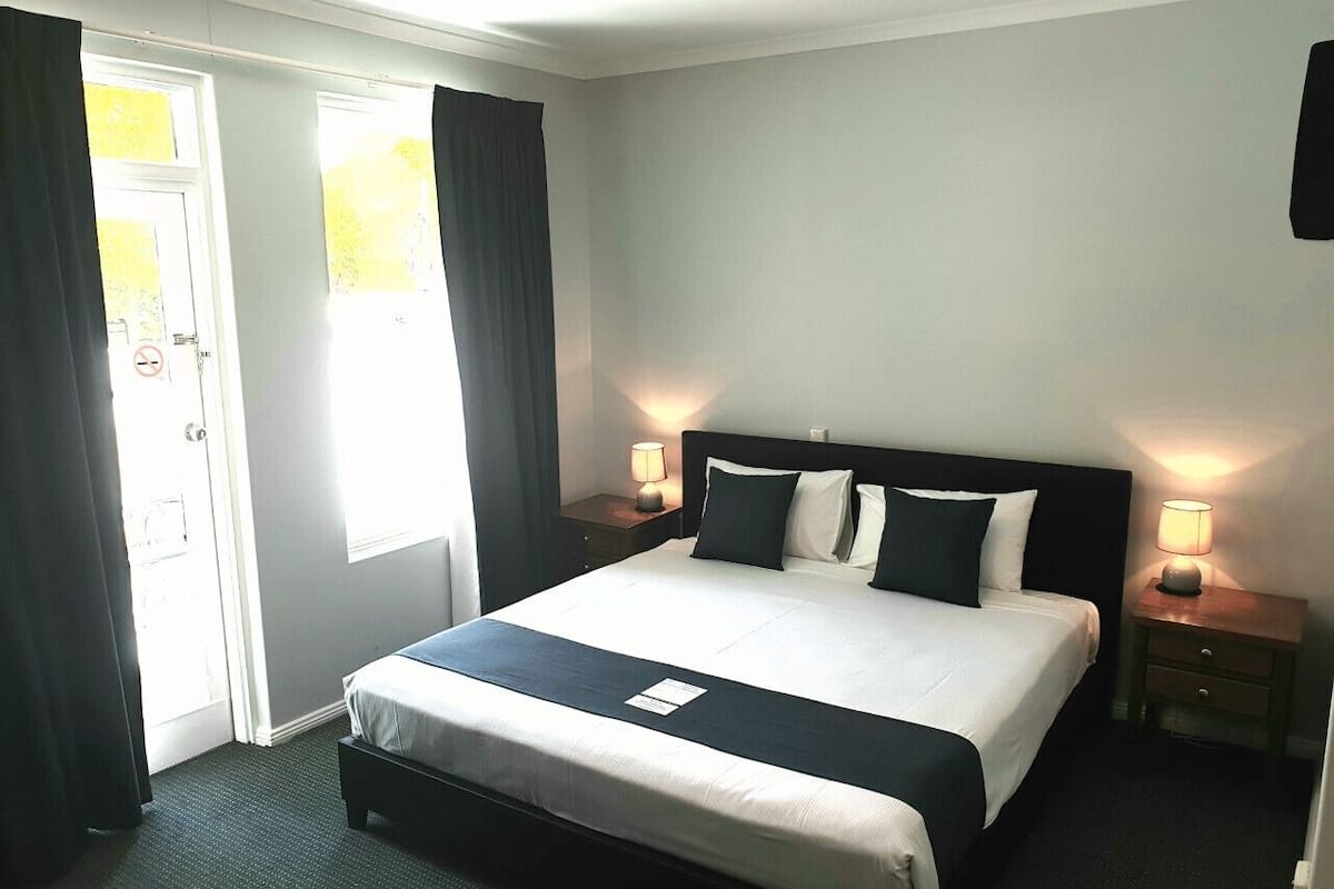 A neatly made bed with a black and white bedspread, two bedside lamps, and a window with curtains.