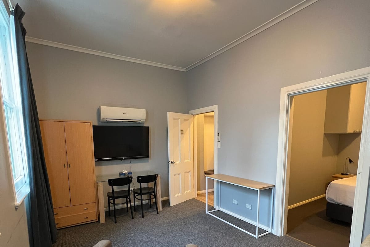 A compact hotel room with a sofa, a small desk, a television, and a bed.