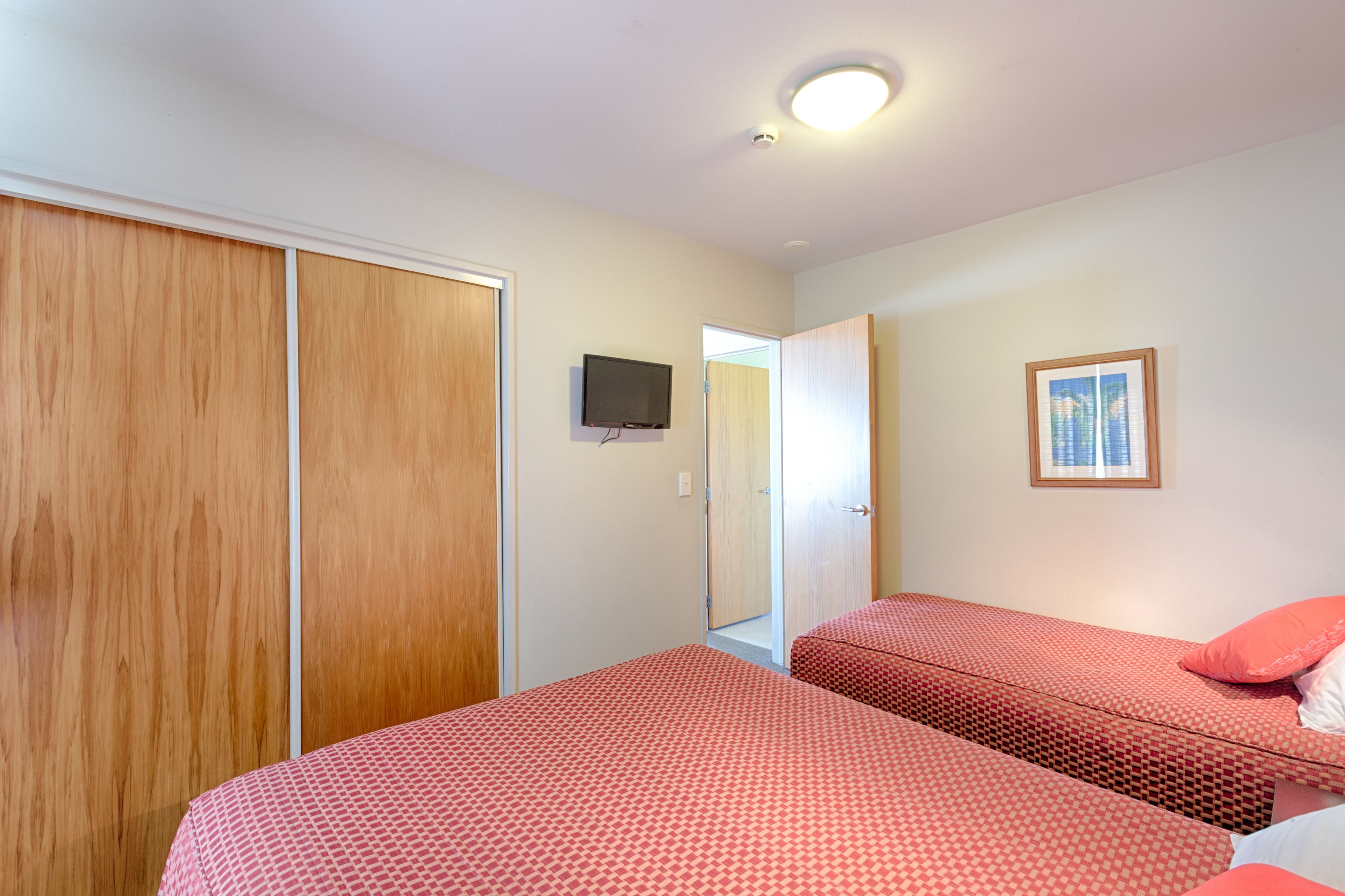 Quarto com duas camas, um guarda-roupa, uma televisão e um quadro na parede.