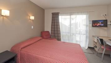 A hotel room with a bed, a desk, a chair, a TV, and a window with curtains.