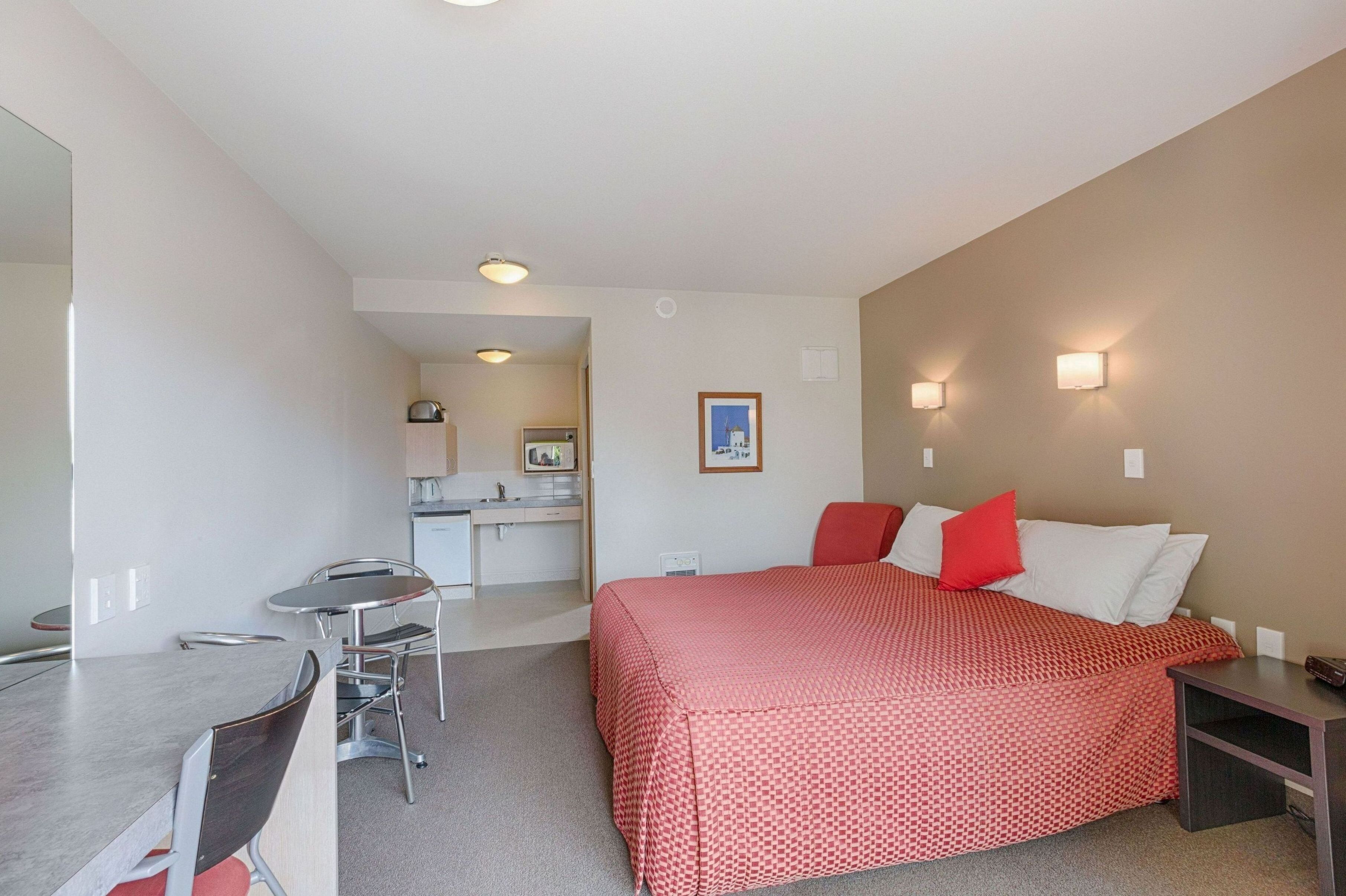 A compact hotel room with a bed, a desk, and a kitchenette.