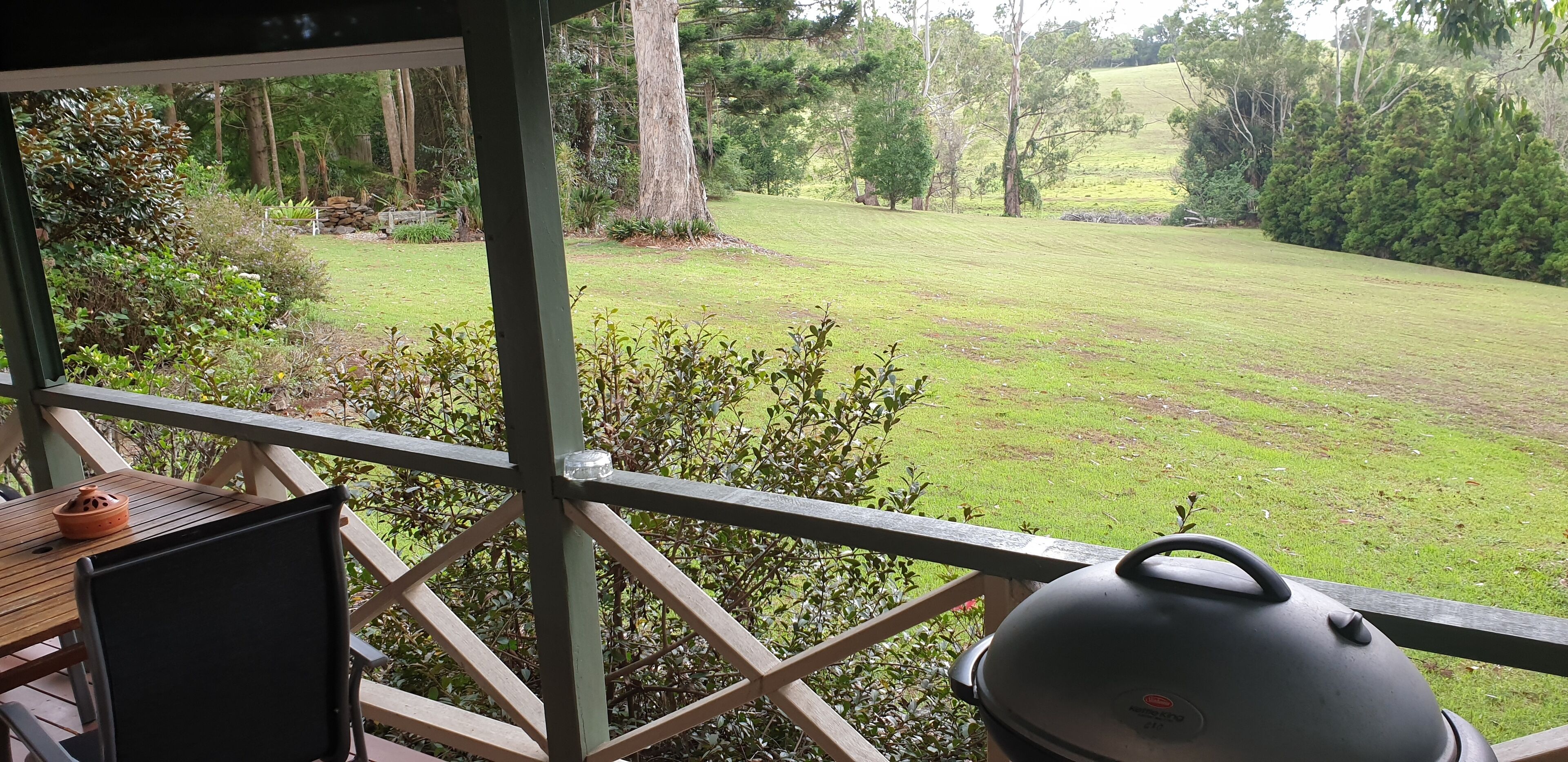 Een overdekt buitengebied met een houten tafel en een barbecue.