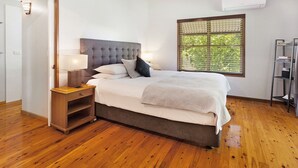 A bedroom with a bed, a nightstand, a window with blinds, and a wooden floor.