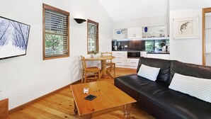 A modern living room with a wooden coffee table, a black leather sofa, and a dining area with a wooden table and chairs.