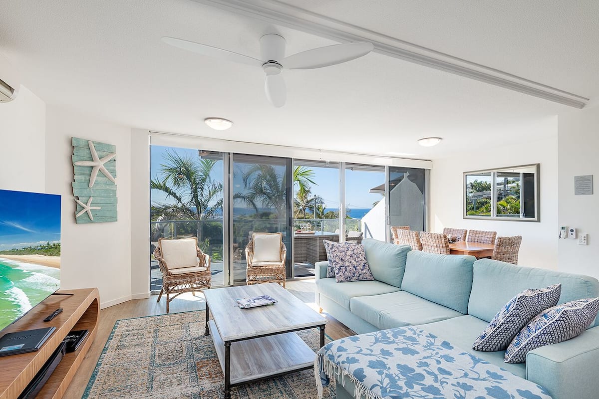 A spacious living room with a light blue sofa, wicker chairs, and a wooden coffee table.