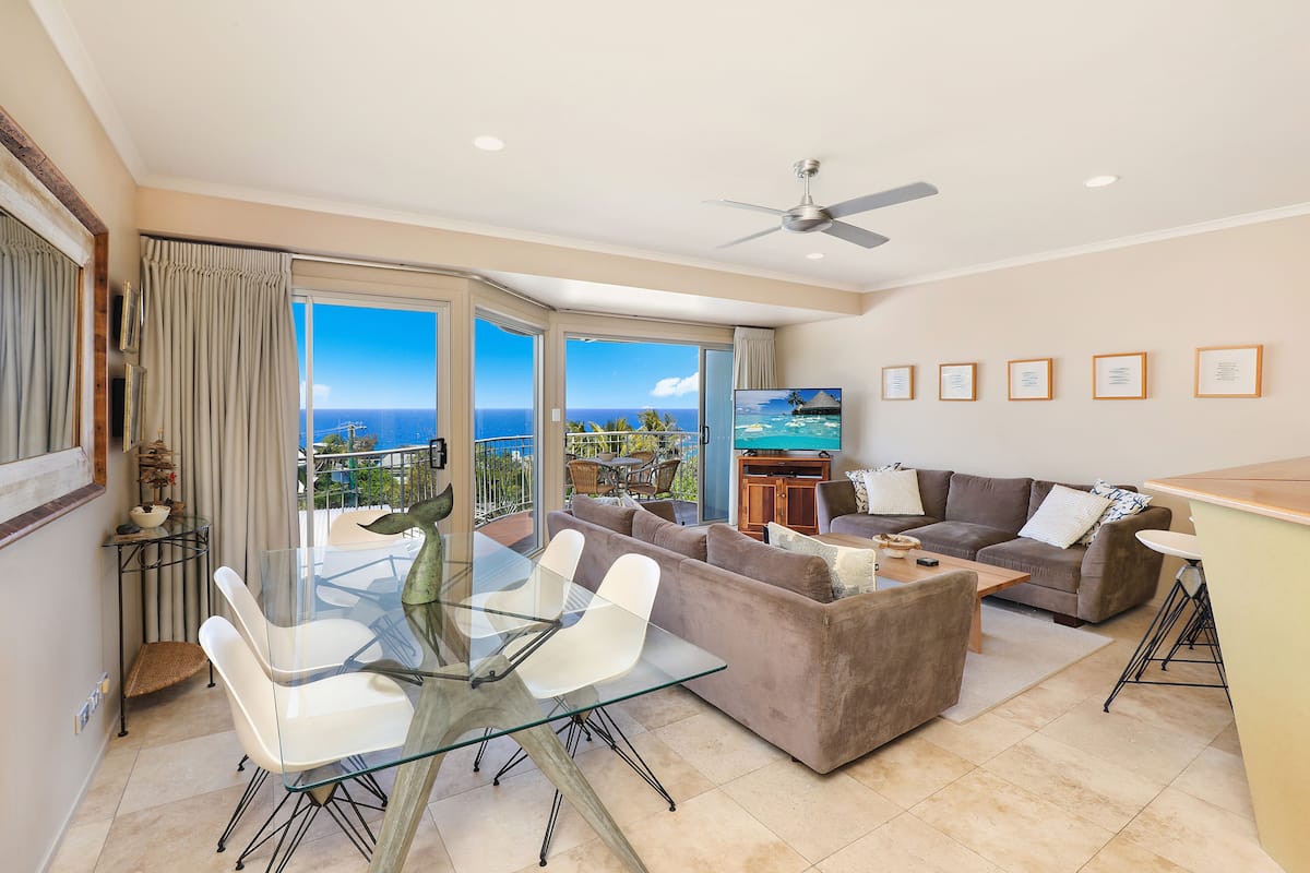 A spacious living area with a glass dining table, a sofa, and a TV.