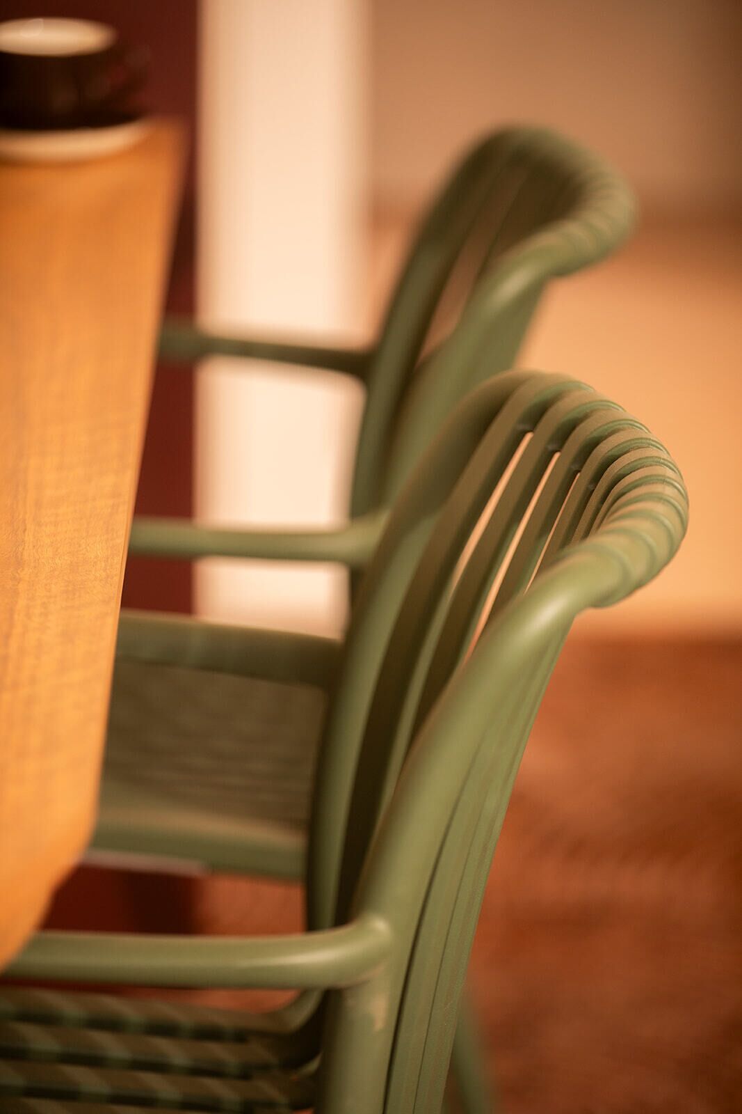 A close-up of a green chair with a woven backrest and a wooden table with a black lid.